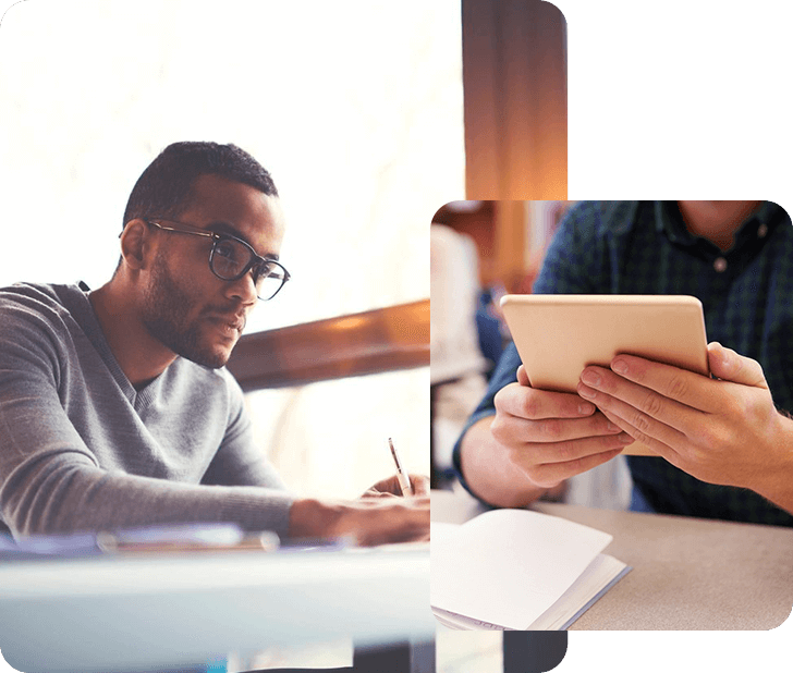 Two men sitting at a table with papers and one man holding an ipad.